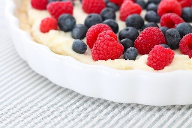 A close up of a lemon berry tart in a white pan on a striped surface