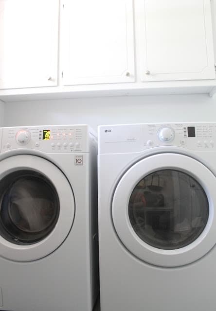 A washer and dryer in a mudroom laundry room with white cabinets.