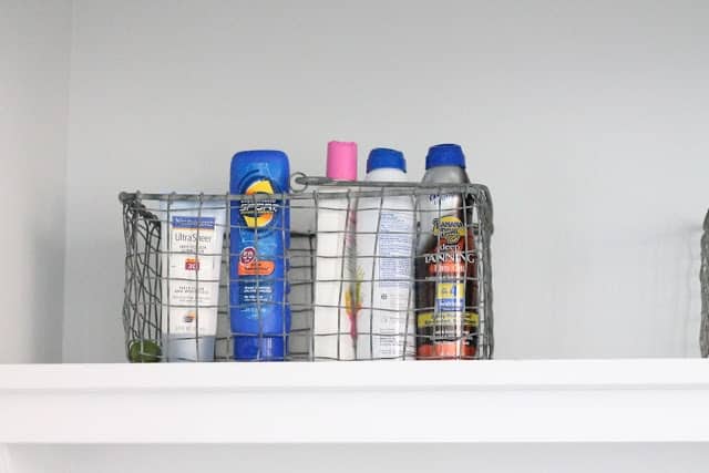 A basket full of sunscreen on the shelf of a mudroom laundry room combination space.