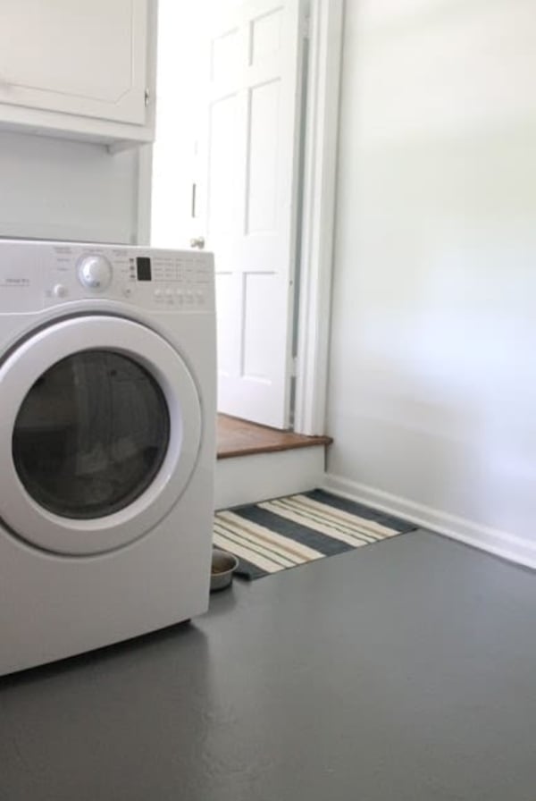 A laundry room with a white washing machine, white cabinets, and gray painted concrete floors