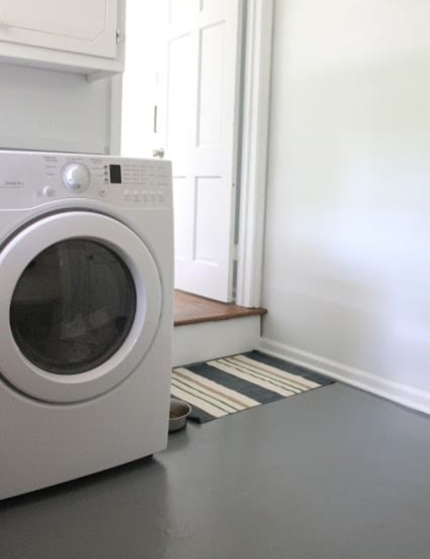 A laundry room with a white washing machine, white cabinets, and gray painted concrete floors