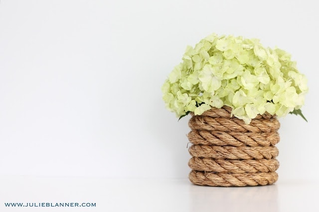On half of the picture, the nautical rope vase filled with light green hydrangeas is seen, while the other side is just a white background.
