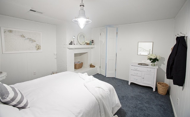 A white bedroom with blue carpet and various knick knacks around on shelves.