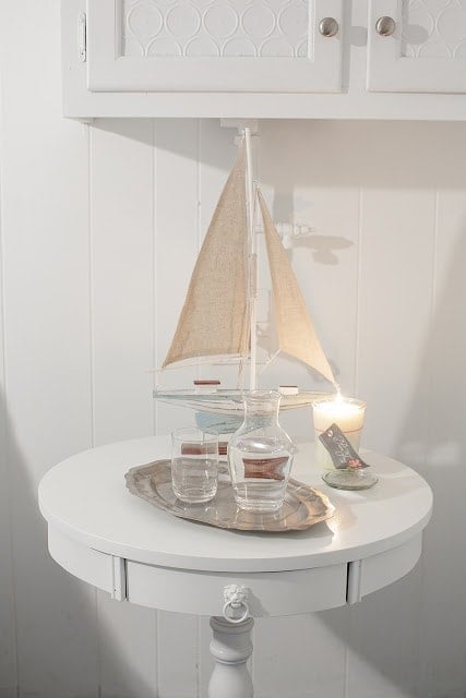 A close up of a side table with a candle, small boat figurine, and water glass. 