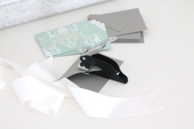 Cards, envelopes, ribbons, and a hole puncher on a white surface.