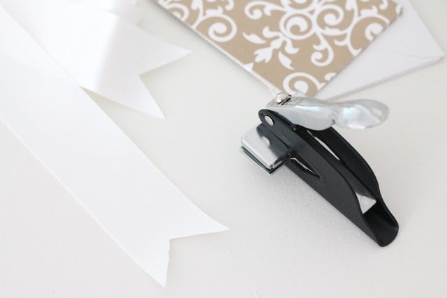 Cards, envelopes, ribbons, and a hole puncher on a white surface.