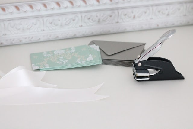 Cards, envelopes, ribbons, and a hole puncher on a white surface.