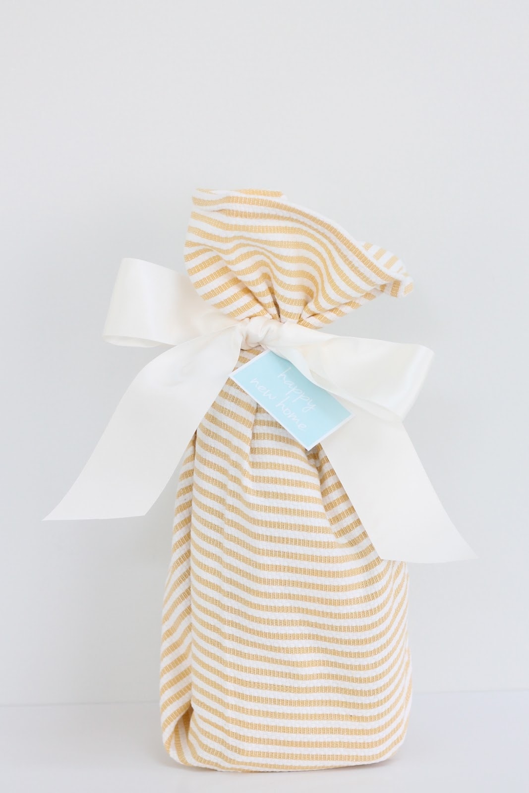 A housewarming gift wrapped in a tea towel and tied with a gift card