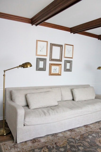 A gallery wall full of a variety of gold gilded frame over a linen sofa.