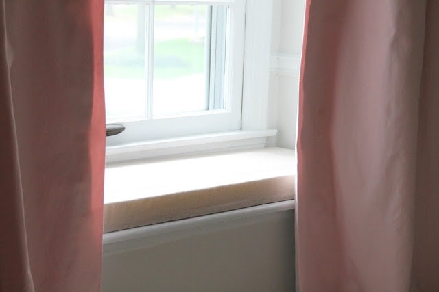 A bedroom with light pink curtains.