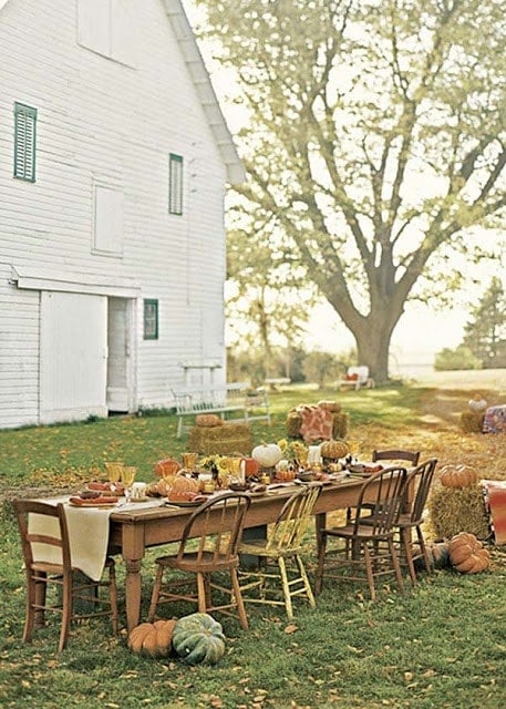 wood farmhouse table covered in pumpkins in front of farmhouse