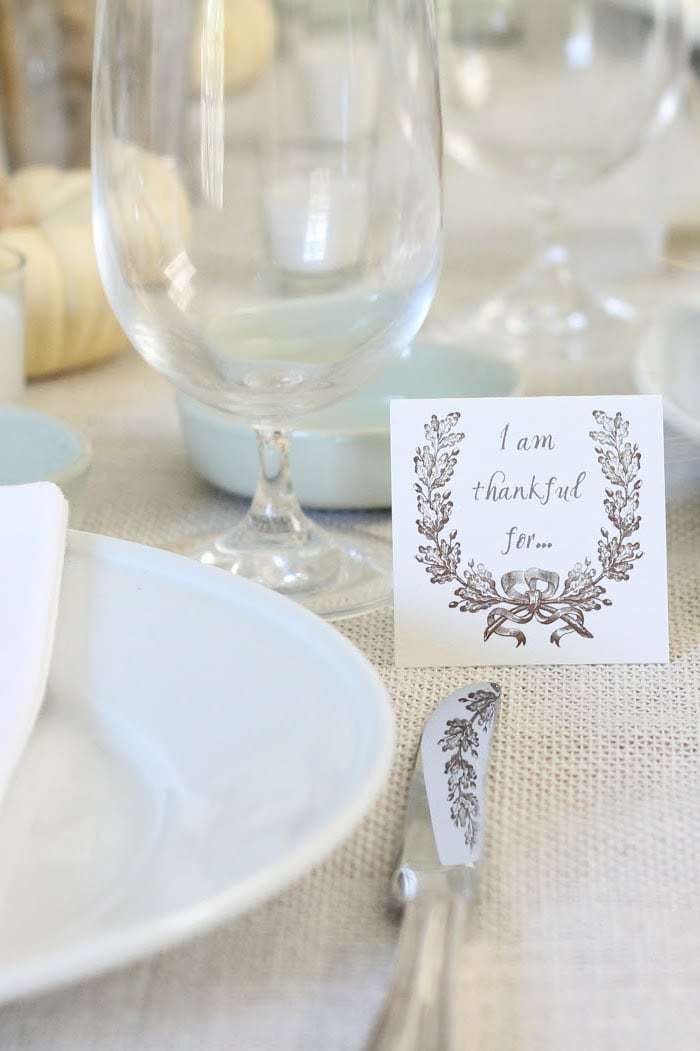 A Thanksgiving table set with white plates, clear glasses and a small place card stating "I am thankful for". 