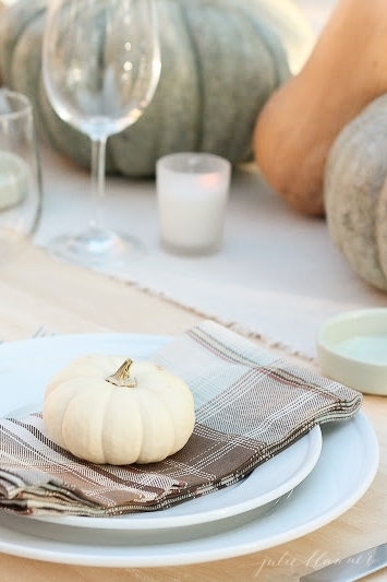 A set thanksgiving table with mini pumpkins as plate garnishes.