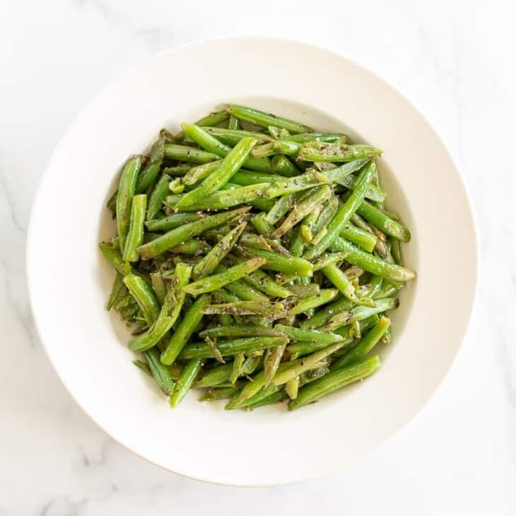 A white bowl full of seasoned green beans.