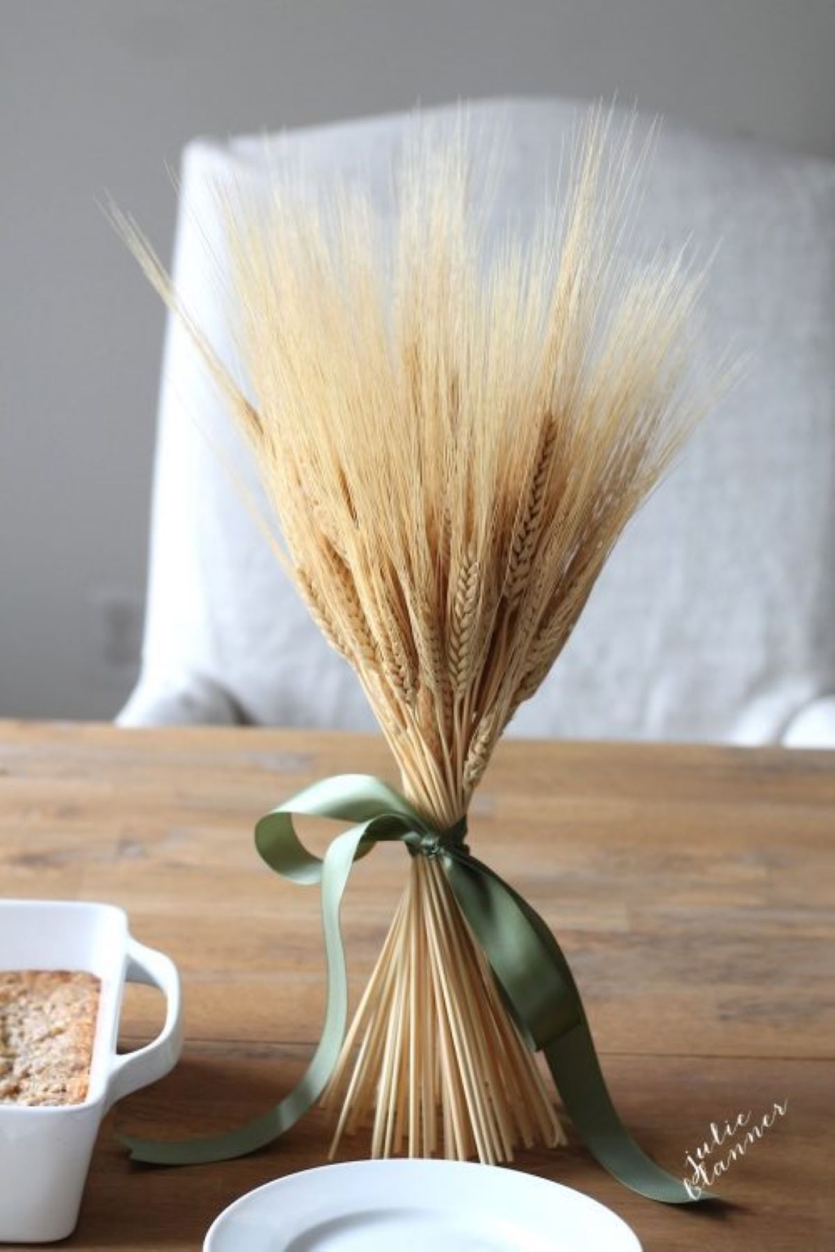 A wheat sheaf tied with green ribbon on a fall table.