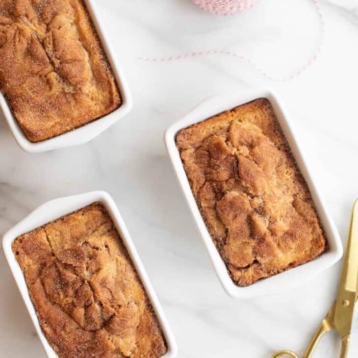 3 cinnamon bread loaves in white miniature loaf pans with red bakers twine and gold scissors