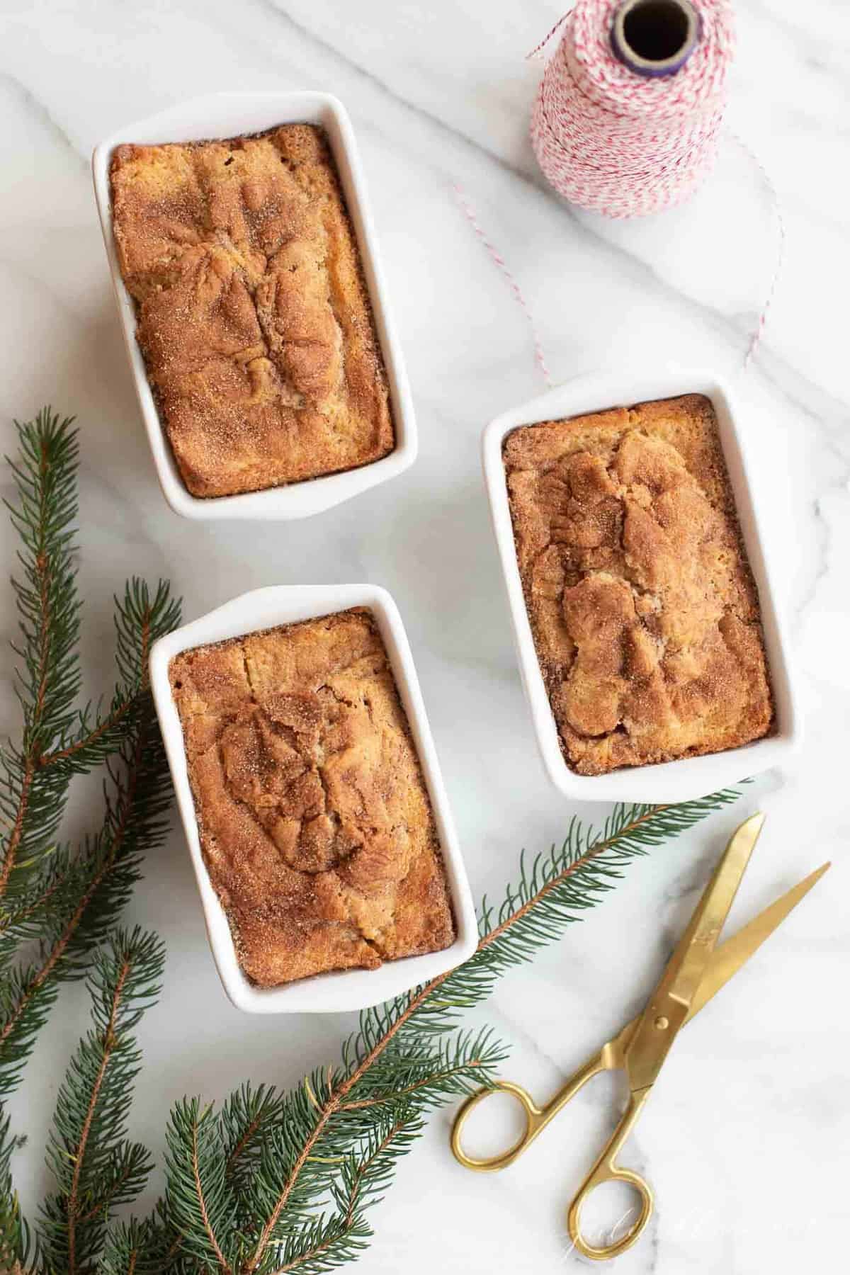 cinnamon bread in white loaf pans by christmas greenery gold scissors and red bakers twine