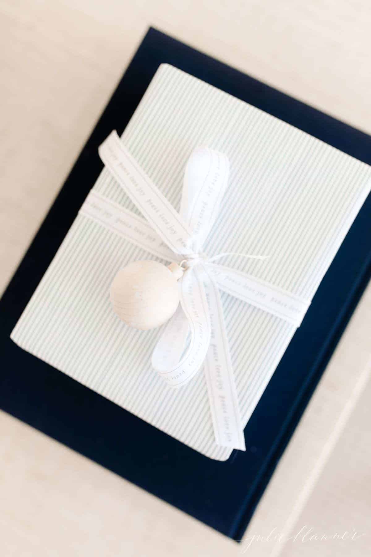 A blue and white christmas gift wrapping box tied with a bow, on top of a navy blue book.