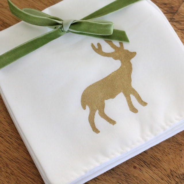 A white napkin with a gold deer tied with green velvet ribbon. 