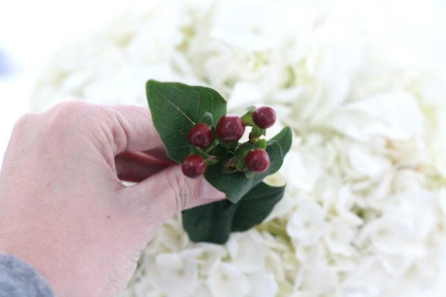 A person holding red berry accents to put into white flowers.