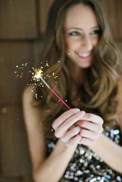 A woman smiling behind a sparkling candle on New Year's Eve.
