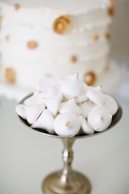 A plate of white cookies in front of a white and gold polka dot New Year's Eve cake.