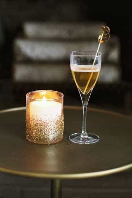 A single glass of champagne next to a glittered votive candle.