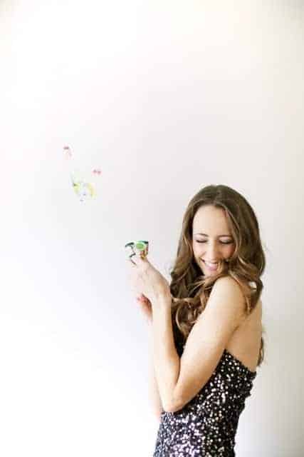 A woman in a black sequined dress holding a confetti popper for a new year's eve party idea.