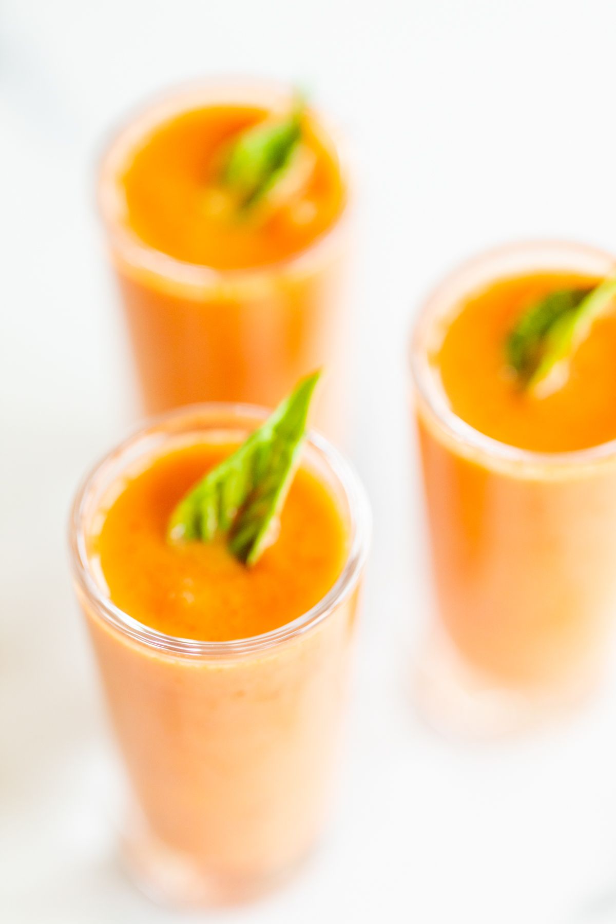 Small glass shooters of creamy tomato soup garnished with fresh basil.