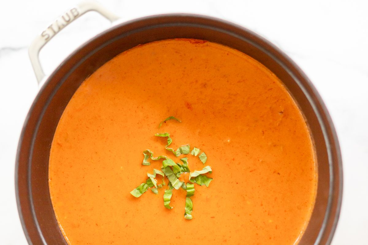 A cast iron pot filled with creamy tomato soup, garnished with fresh basil.