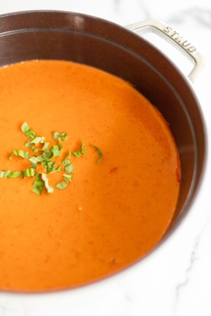 A cast iron pot filled with creamy tomato soup, garnished with fresh basil.
