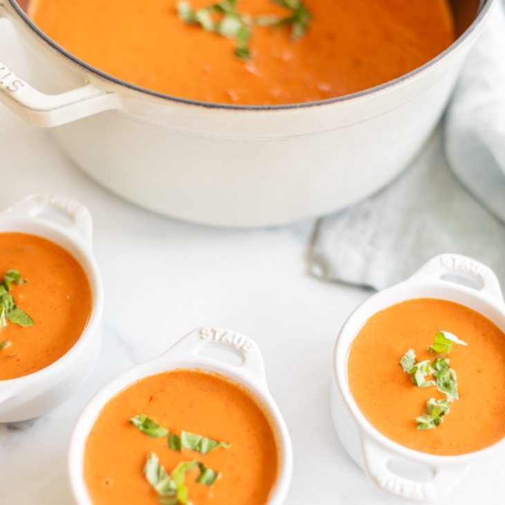 A cast iron pot filled with creamy tomato soup, garnished with fresh basil. Bowls of soup to the side.