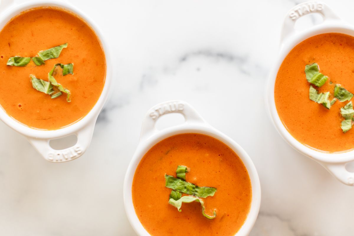 Three white bowls of creamy tomato soup on a marble countertop.