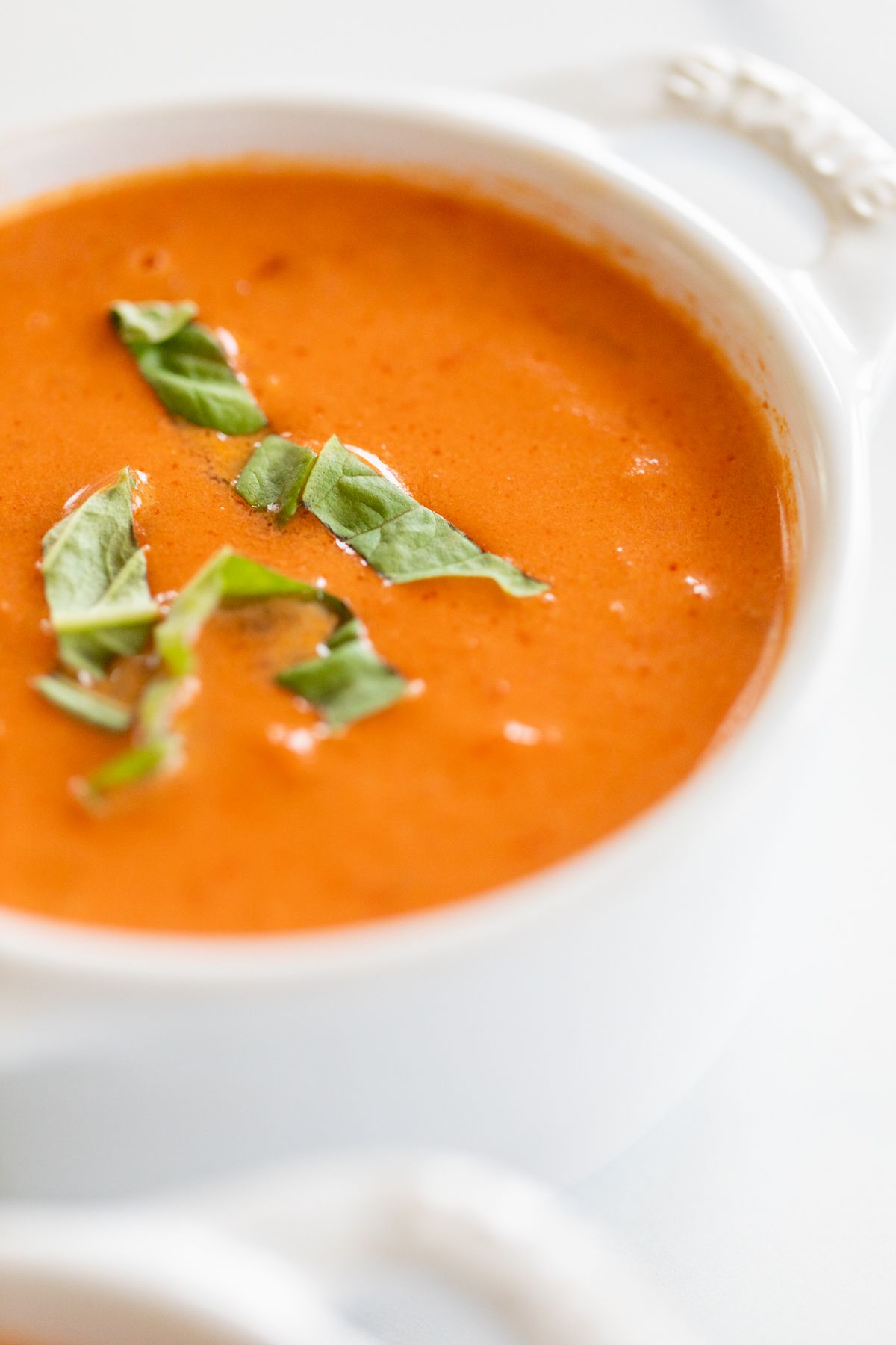 A white bowl full of a creamy tomato soup recipe, garnished with fresh basil.