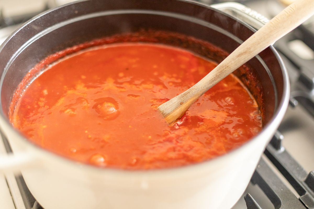A cast iron pot on a stovetop with creamy tomato soup inside.