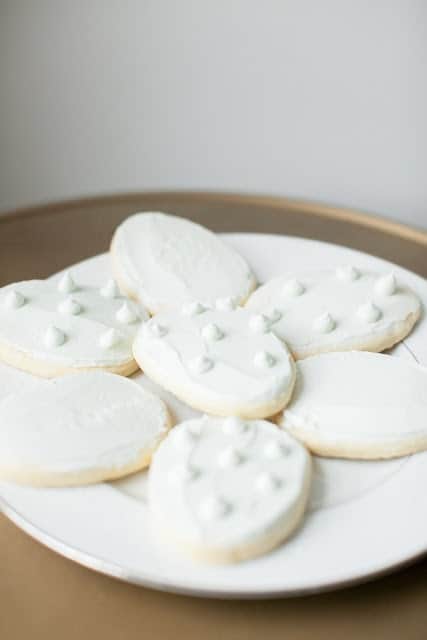 A white plate full of white frosted easy sugar cookies for Easter in the shape of eggs.
