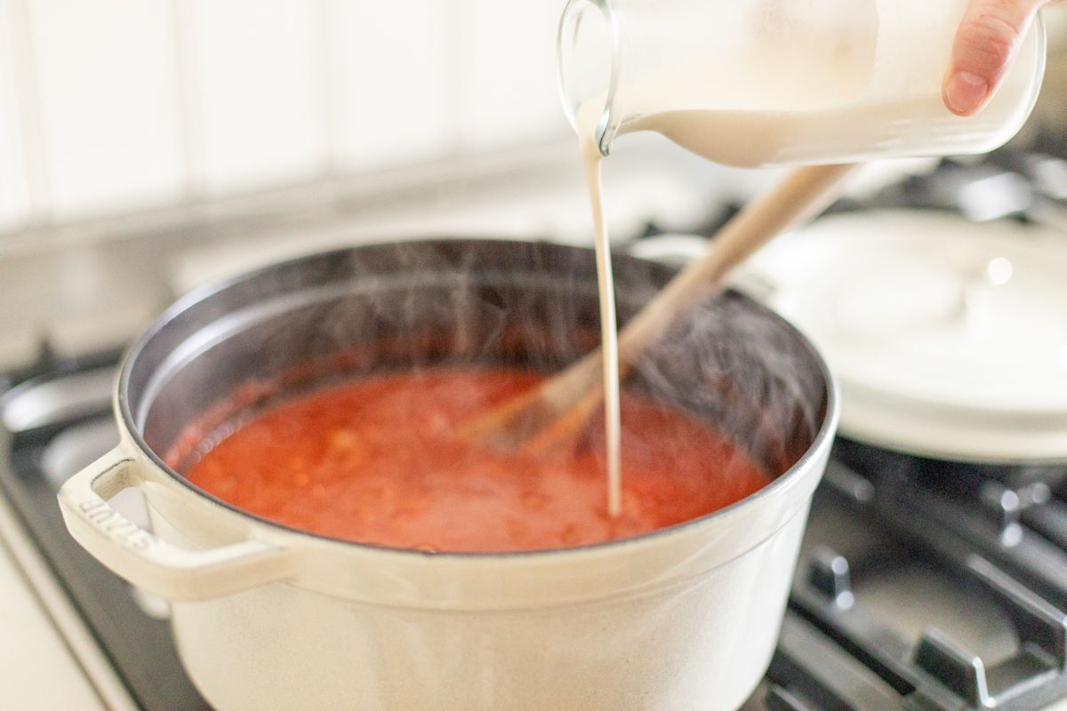 A cast iron pot on a stovetop with creamy tomato soup inside.