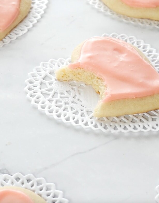 easy sugar cookies in a cutout heart shape on a marble surface, one has a bite taken out!