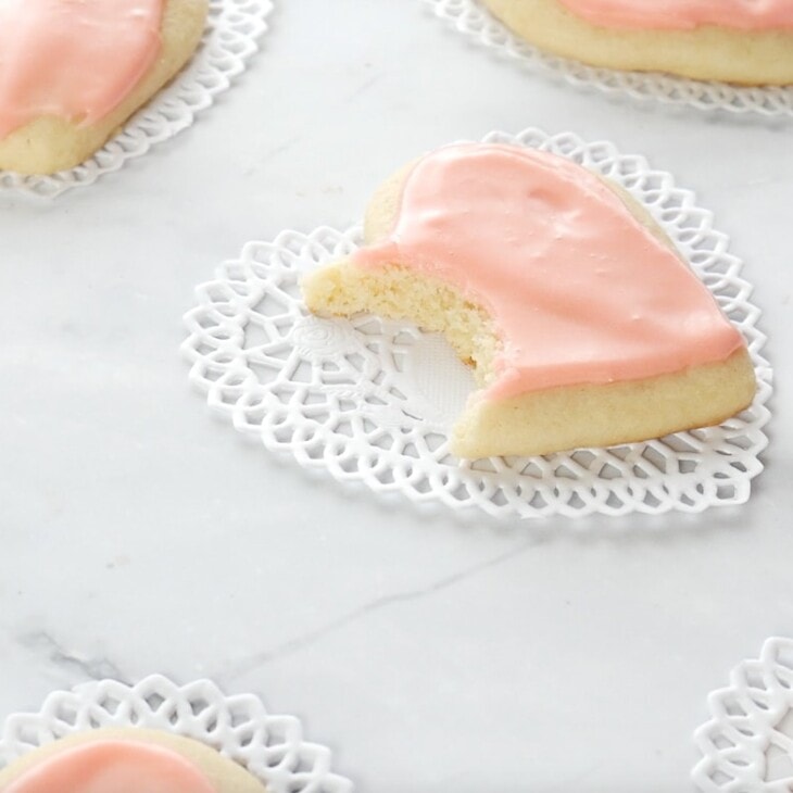 easy sugar cookies in a cutout heart shape on a marble surface, one has a bite taken out!