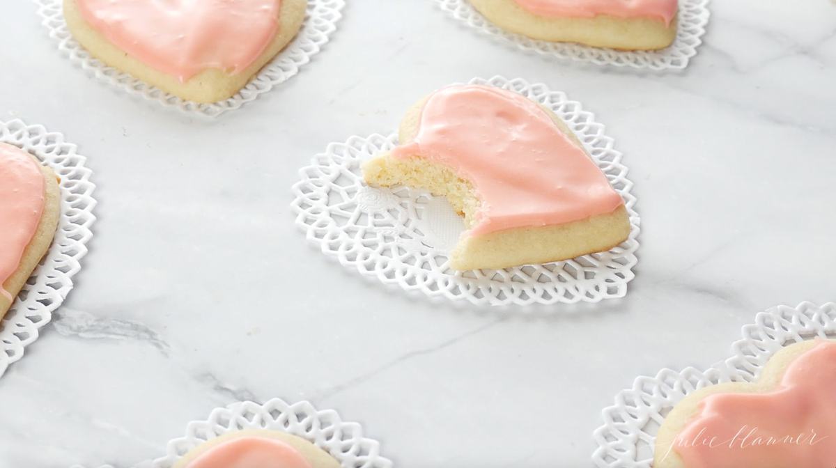 Pink heart shaped sugar cookies on a marble surface on heart shaped paper doilies.