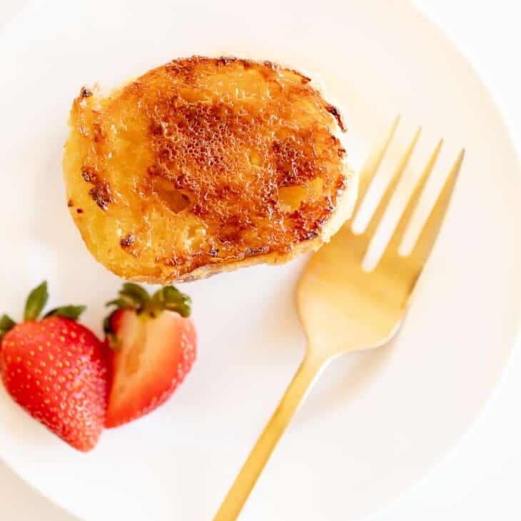 slice of creme brulee french toast on white plate with gold fork and strawberries