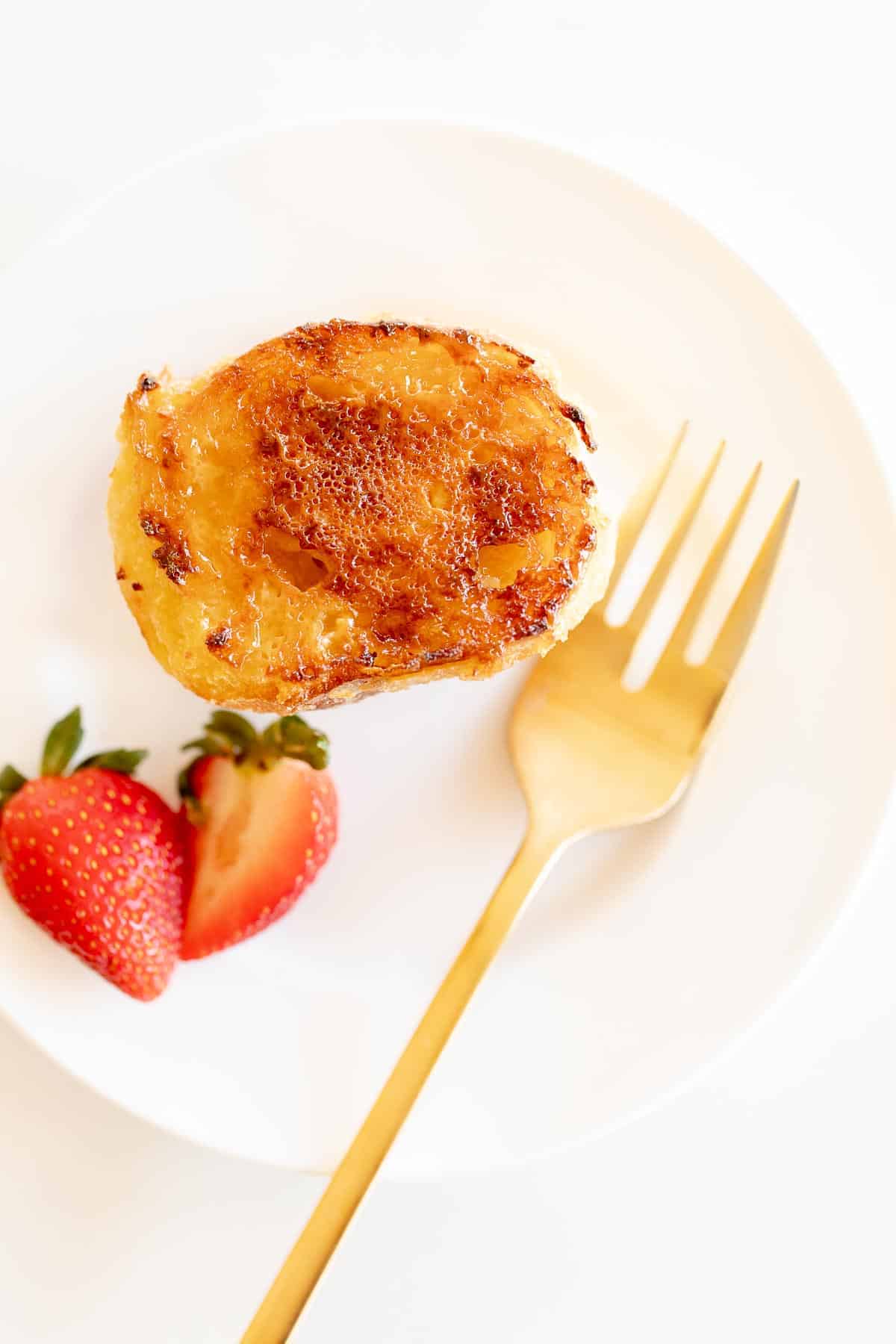 slice of creme brulee french toast on white plate with gold fork and strawberries