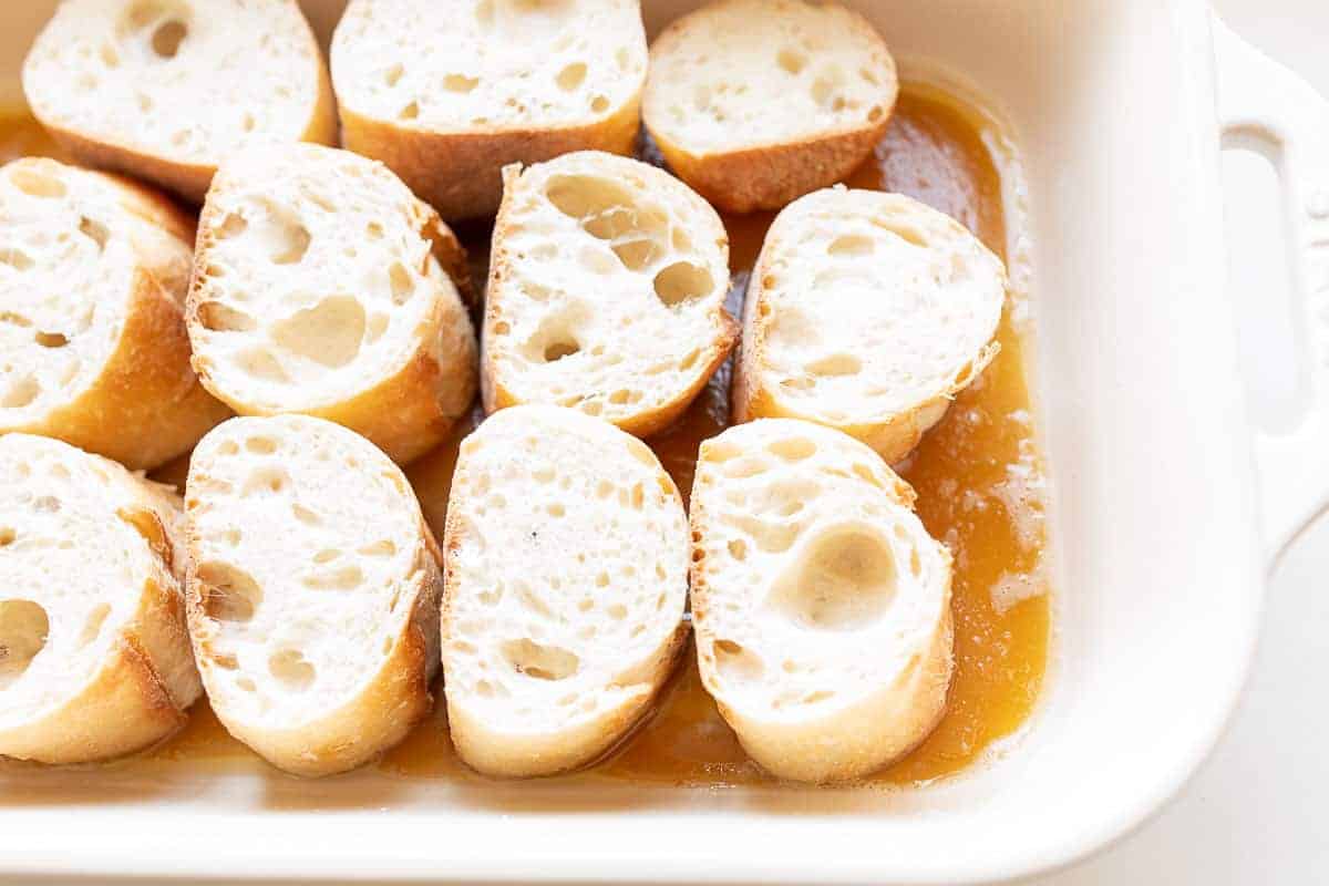 slices of french bread soaking in caramel sauce in casserole dish