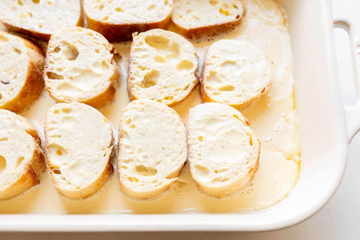 slices of french bread soaking in custard in a casserole dish
