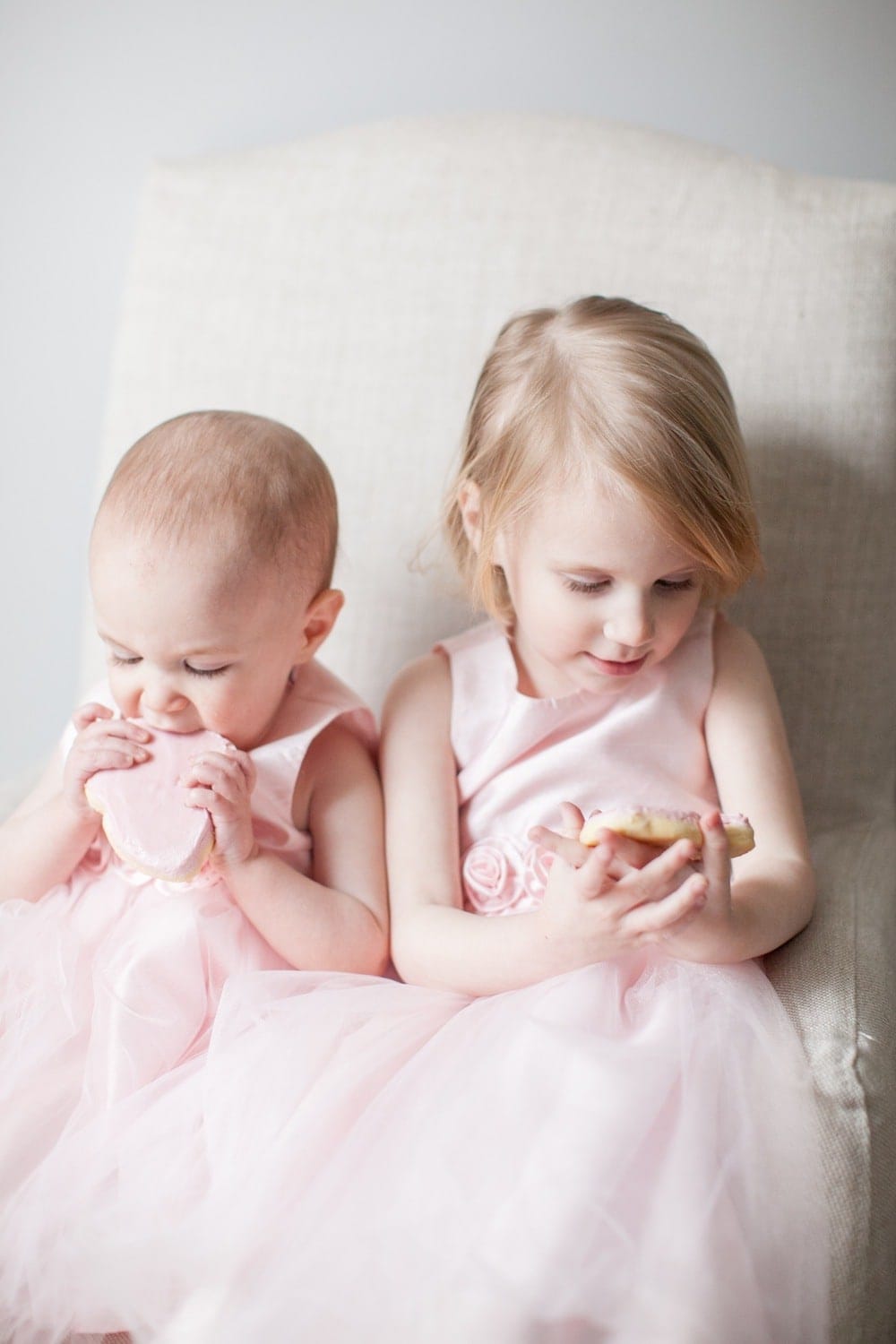 Two little girls wearing matching dresses sitting next to each other.