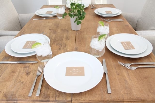 Table with simple white place settings, potted clover centerpiece, and handwritten place cards.