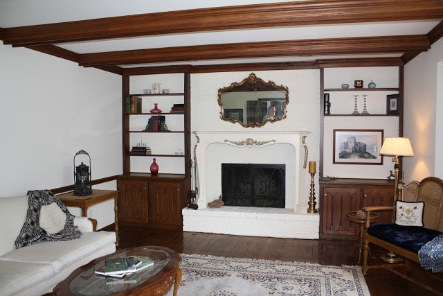 A living room filled with furniture, shelves, and a fireplace, before being redone.