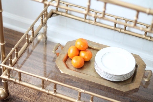 A gold bar cart decorated with plates and serving dishes for a party.