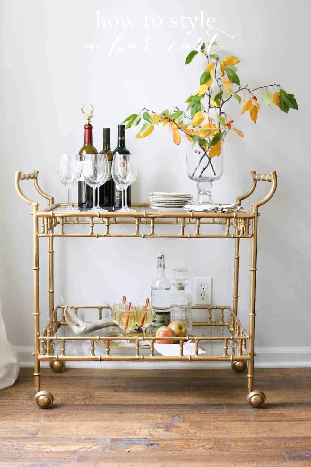 A brass bar cart with liquor bottles and glassware on top.