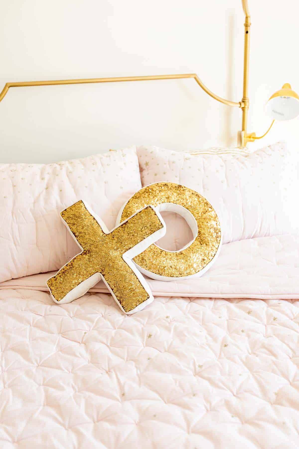 Sequined XO gold pillows on pale pink bedding on a gold bed.